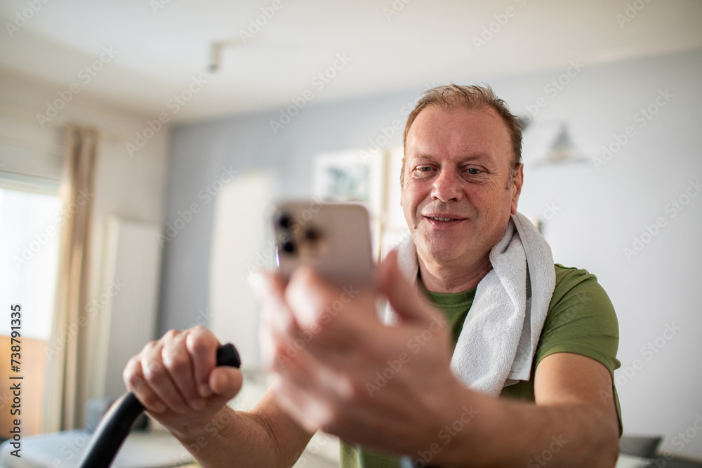 © Marko Geber - Middle aged man using smartphone on home exercise bike © Marko Geber - Middle aged man using smartphone on home exercise bike