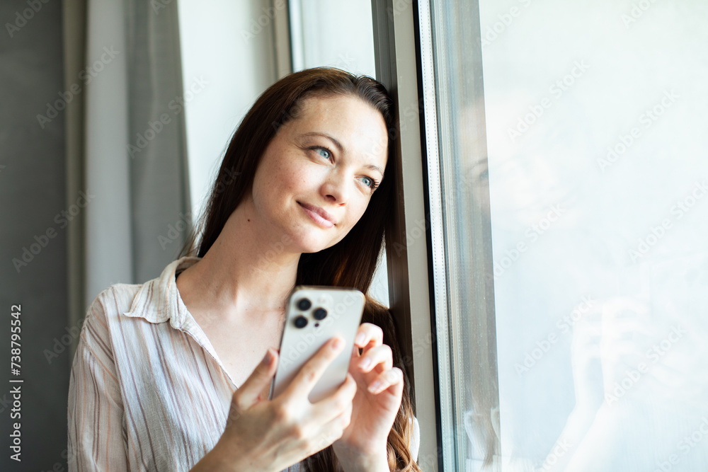 Young woman using smartphone by the window at home Young woman using smartphone by the window at home