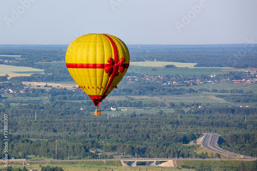 A yellow-red balloon in the form of a gift flies over the countryside. Summer day. Balloon flight.