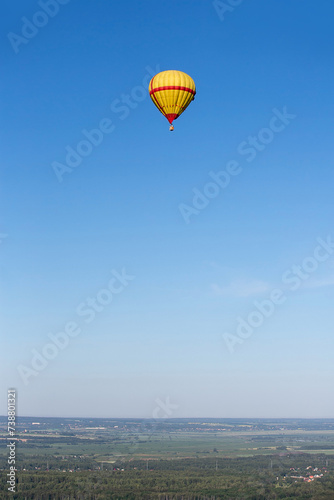 A yellow-red hot air balloon flies high in the sky over the countryside. Summer day. Balloon flight.