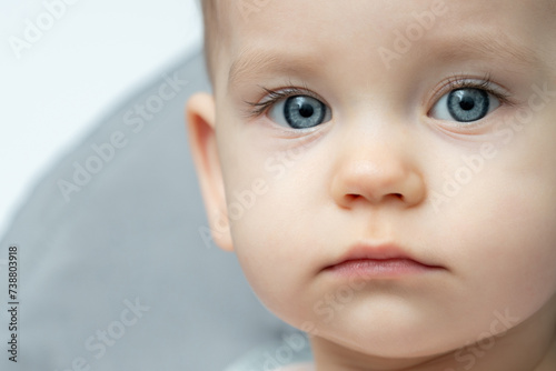 Close up of a babys face with blue eyes, looking at the camera