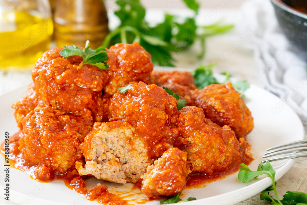 Classic Italian meatballs with tomato sauce on white plate and rustic background.