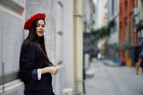 A woman standing near a wall in the city wearing a stylish jacket and a red beret with red lips, traveling. © SHOTPRIME STUDIO