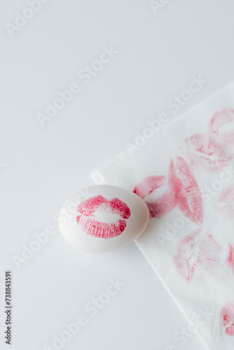 white Easter egg with a red lipstick print on a white background, next to it is a napkin with many lip prints