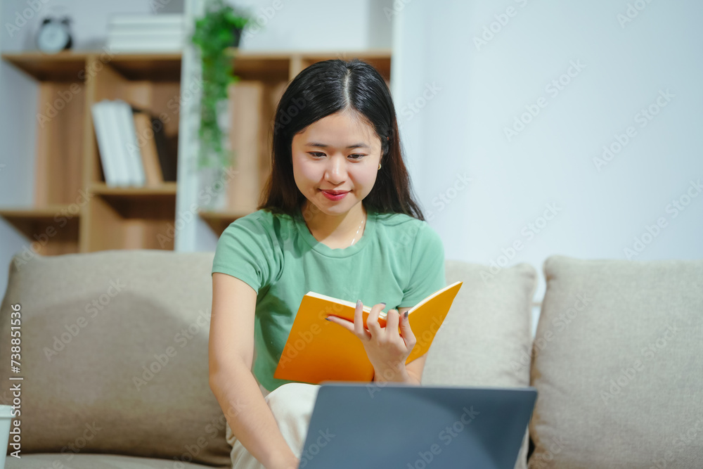 young Asian girl engages in online learning, doing homework on her sofa in the living room. video classes, combining comfort and education at home. young Asian girl engages in online learning, doing homework on her sofa in the living room. video classes, combining comfort and education at home.