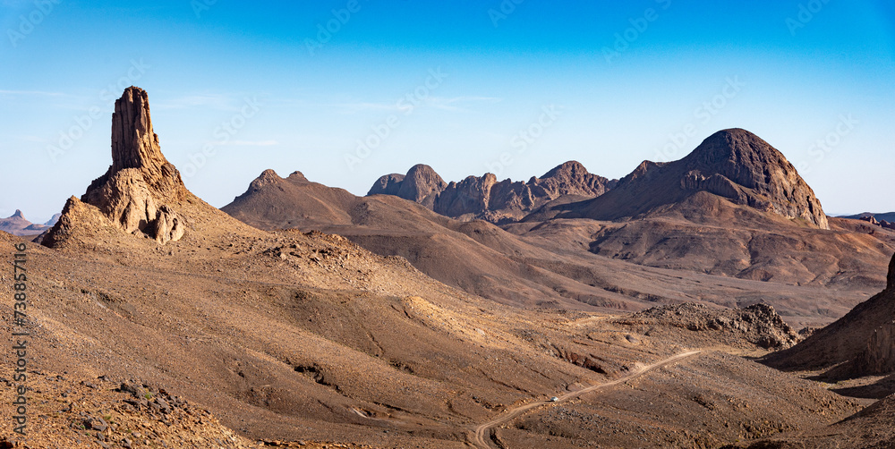Naklejka premium Hoggar landscape in the Sahara desert, Algeria. A view of the mountains and basalt organs that stand around the dirt road that leads to Assekrem.