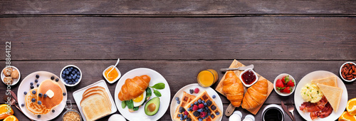 Breakfast or brunch bottom border on a dark wood banner background. Top down view. Assorted sweet and savory food items.