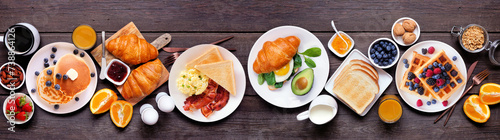 Breakfast or brunch table scene on a dark wood banner background. Top view. Assortment of sweet and savory food items.