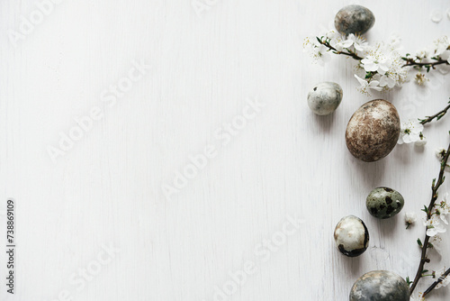 Easter flat lay. Stylish easter eggs and cherry blossom on rustic white table. Happy Easter! Minimal easter border template with space for text. Modern natural dye marble eggs and spring flowers