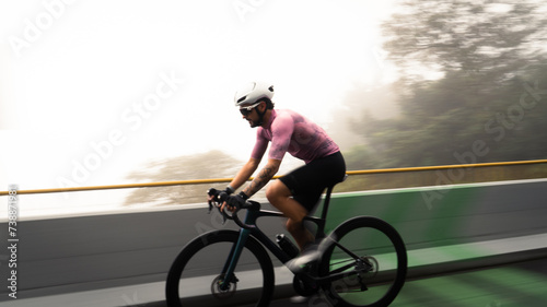 male cyclist with white helmet and pink t-shirt in side view riding bike on a famous street in colombia on a cold and foggy day. Dynamic and moving picture
