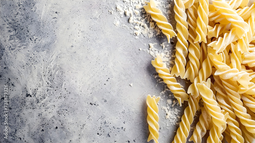 Raw pasta fusilli with flour on grey background, top view