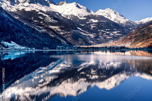 Panorama of the snow-capped Swiss Alps reflecting on the clear waters of a lake under the blue sky on a sunny day