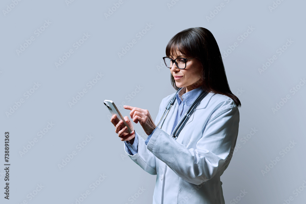 Profile portrait of female doctor using smartphone on gray background Profile portrait of female doctor using smartphone on gray background