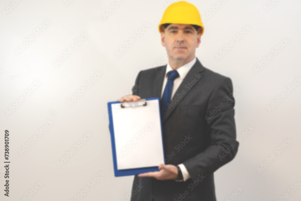 A man in a helmet holds a folder with a white sheet in his hands. A man holding a folder over isolated background, blurry photo A man in a helmet holds a folder with a white sheet in his hands. A man holding a folder over isolated background, blurry photo
