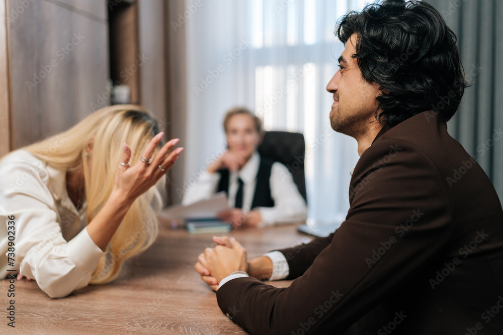 Married couple quarreling in front of family psychologist. Angry wife quarreling with sad husband during couple counseling. Unhappy couple having marriage counseling sitting at table in office. Married couple quarreling in front of family psychologist. Angry wife quarreling with sad husband during couple counseling. Unhappy couple having marriage counseling sitting at table in office.