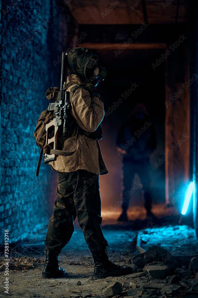 a man in military uniform with a weapon, a gas mask on his face, stands in a gloomy destroyed building