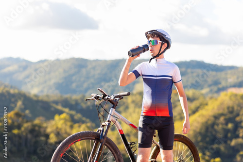 Brazilian cyclist enjoying a break atop a mountain, hydrating with water while soaking in nature's tranquility. Ideal for those seeking a healthy lifestyle with outdoor exercise