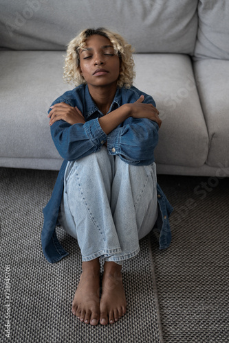 Mentally burntout,devastated and depressed young woman sits near couch with her head in her hands. Meantal health issues concept. Vertical banner photo