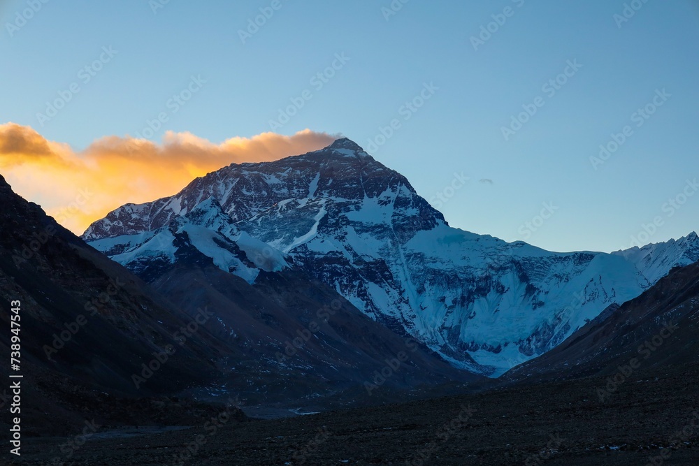 Fototapeta premium Experience the breathtaking spectacle of sunrise over Mt. Everest as its towering silhouette casts a majestic shadow against the dawn-lit sky, while vibrant crimson hues dance atop the veiling clouds.