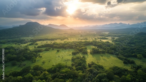 A serene ecoregion of lush green fields and towering mountains, kissed by the vibrant hues of a stunning sunrise and scattered with vibrant vegetation © ChaoticMind