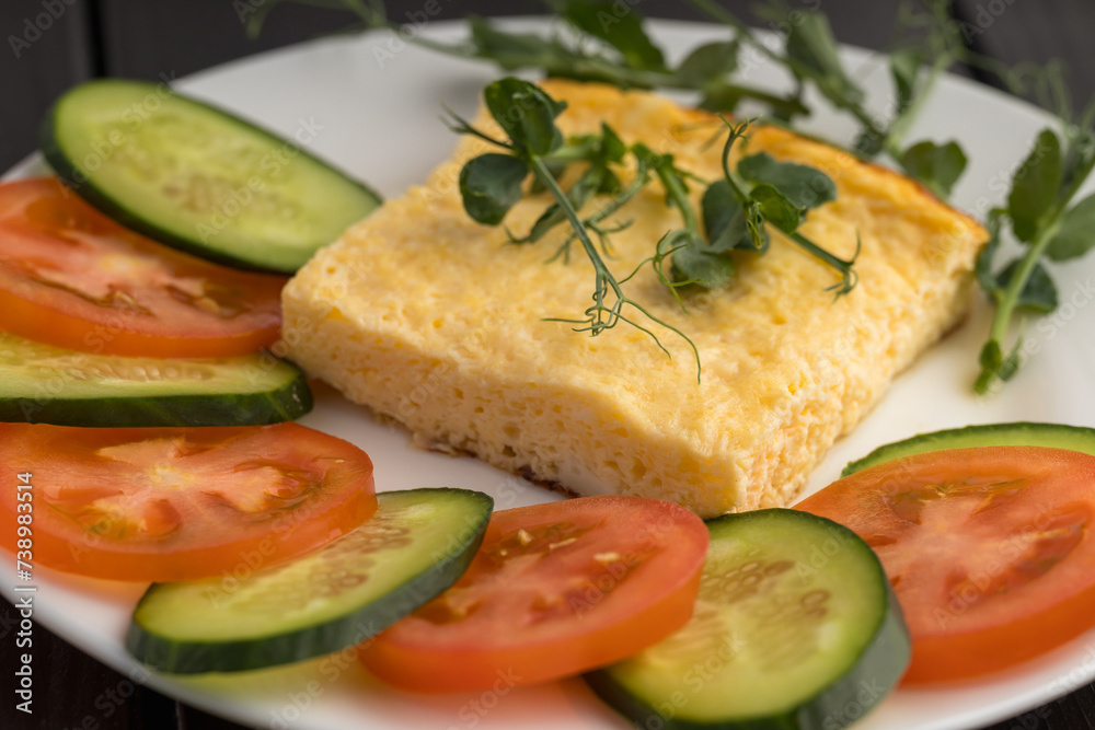 A white plate with a quiche slice, and fresh slices of tomato and cucumber, garnished with pea shoots A white plate with a quiche slice, and fresh slices of tomato and cucumber, garnished with pea shoots