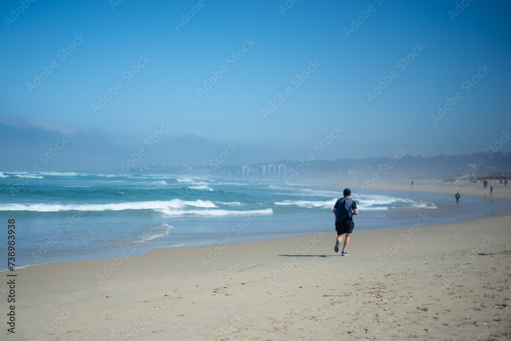 a man with a blue shirt running on the sand during a sunny day