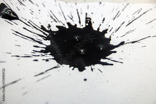 Large black blot with splashes close-up on a white background	
