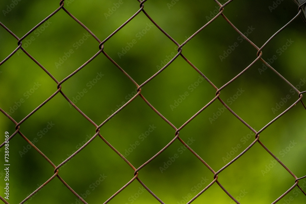 Rusty chain link fence up close with green plant bokeh background Rusty chain link fence up close with green plant bokeh background