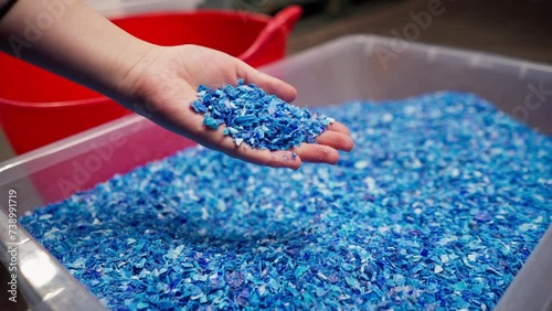 Close-up of shredded plastic lids stored in a special container at a waste recycling station hand holding the product