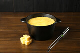Fondue pot with melted cheese, forks and pieces at wooden table