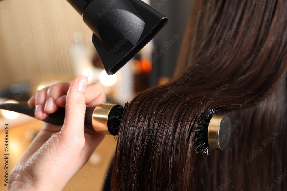 Fototapeta premium Hairdresser blow drying client's hair in salon, closeup
