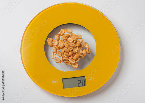 A handful of peanuts weighted on yellow round kitchen electronic scale