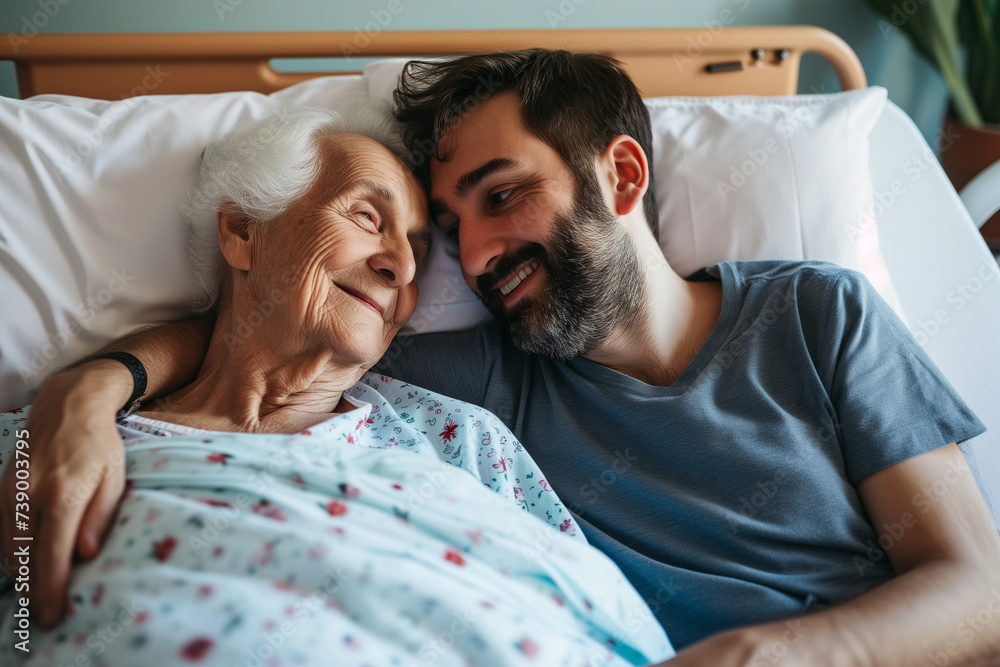 An elderly woman and a middle-aged man are embracing and smiling to each other in a hospital bed. - obrazy, fototapety, plakaty 