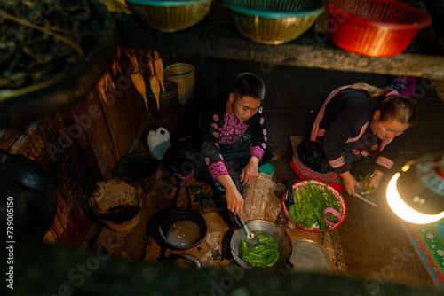 Asian family cooking and having dinner together at home. Hill tribe man and woman in traditional dress cooking food with herbal vegetable in traditional kitchen. Tribal culture and nature food concept