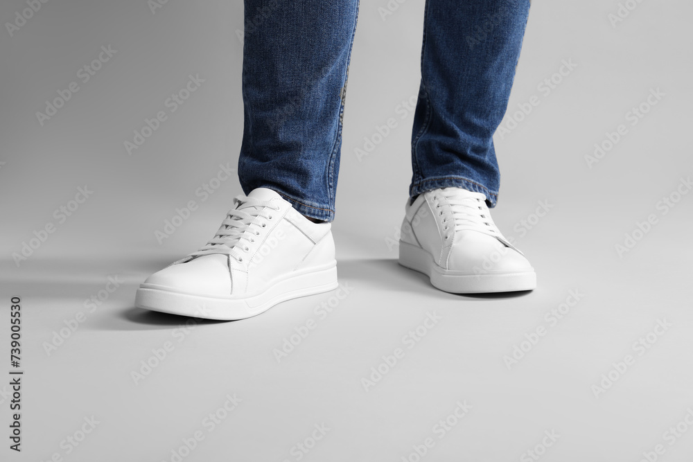 Man wearing stylish white sneakers on grey background, closeup Man wearing stylish white sneakers on grey background, closeup