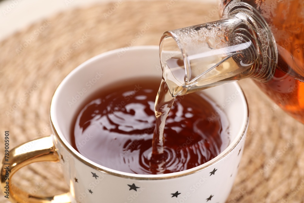 Pouring aromatic tea into cup at table, closeup Pouring aromatic tea into cup at table, closeup