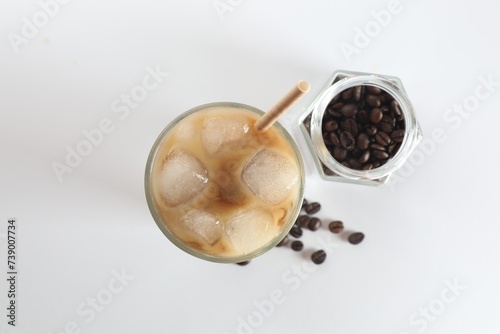 Iced coffee with milk in glass and jar of roasted beans on white background  top view