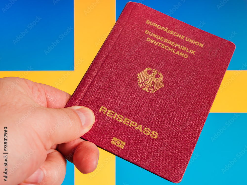 German Passport Held in Hand Against Blue and Yellow Background German Passport Held in Hand Against Blue and Yellow Background