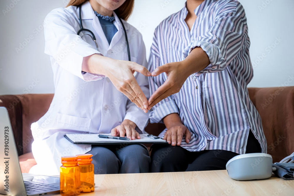 Doctor and patient woman hand do heart shape after explains the bottle of pills on the sofa at home and reports health examination results, medical checkup concept