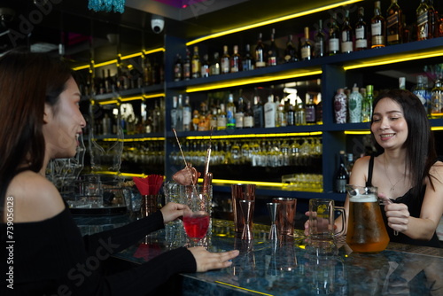 Asian woman works as a bartender, standing at the counter and pouring beer into glasses for Asian female customers to drink in the cocktail lounge.