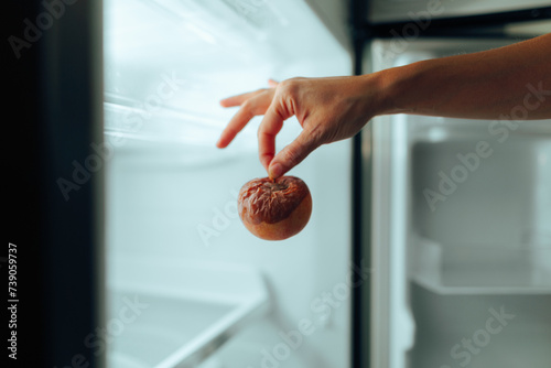 Hand Taking out a Rotten Apple from the Fridge. Person throwing away some damaged foods from a broken refrigerator 
