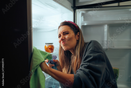 Woman Cleaning her Refrigerator Using a Special Detergent Solution. Stressed girl trying to get the chores done cleaning her fridge  
 photo