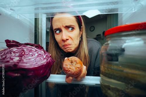 Woman Taking out a Rotten Fruit from her Fridge. Disgusted girl having her stomach turning from bad spoiled foods 

