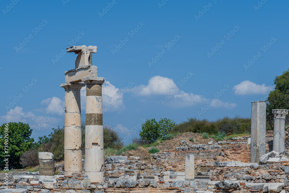 Tall ancient columns stand amidst ruins under a bright clear sky