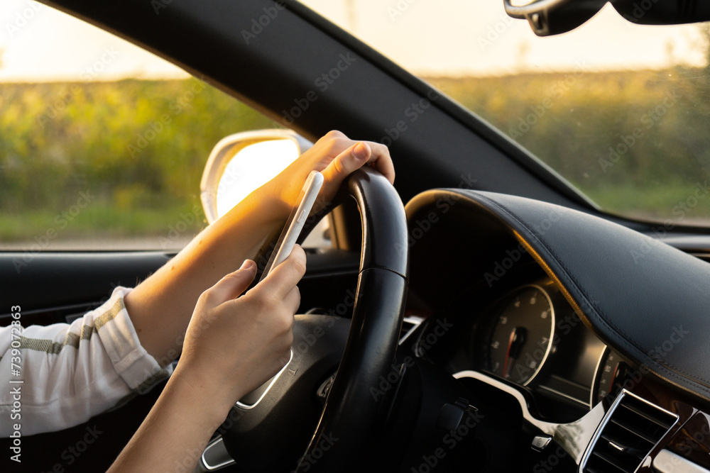 Woman sending messages with smartphone while driving automobile. Female driver using mobile phone on the road during driving the car. Safety and technology concept 