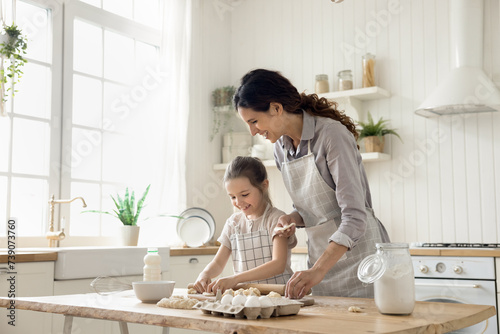 Hispanic woman teach little daughter to cook, prepare homemade dough for pastries, make holiday pie or cookies on weekend leisure in kitchen at home. Natural products, healthy eating, kid development