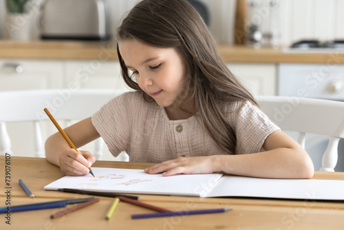 Little girl painting pictures in paper sketchbook with pencils. Cute kid sit at table in cozy domestic kitchen drawing in album, looking focused, enjoy creative activity, favourite hobby alone at home