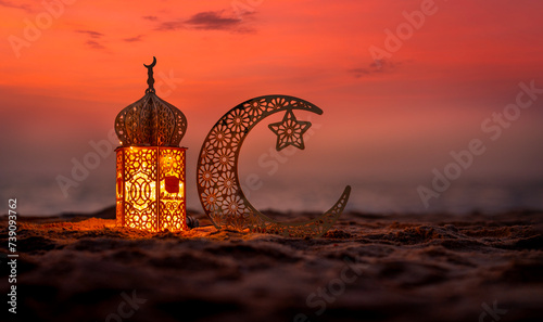 Traditional lantern lamp with crescent moon on the beach during sunset, Ramadan Kareem and Eid Mubarak greeting banner image