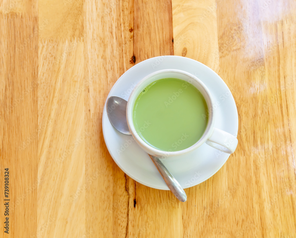 Top view of hot condensed milk matcha green tea served in white cup and small plate with small tea spoon on brown wooken background Top view of hot condensed milk matcha green tea served in white cup and small plate with small tea spoon on brown wooken background