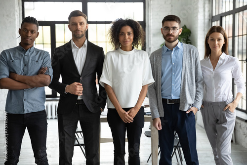 Group portrait of aspiring young coworkers. Confident start-up company employees at work standing together and looking at camera. Staff members of multinational organization in modern workspace photo
